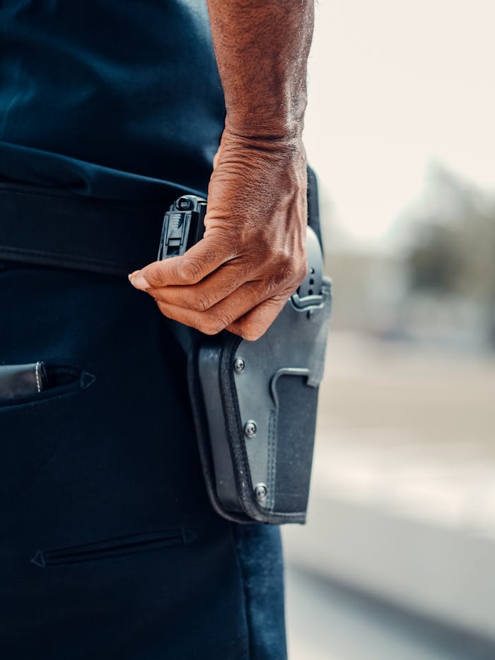person-holding-a-gun-in-a-holster-7714760 A police officers hand gripping the holster of a handgun, symbolizing readiness and security.