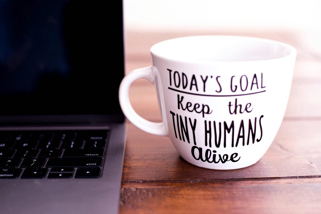 Close-up of a mug with motivational text beside a laptop on a wooden desk.