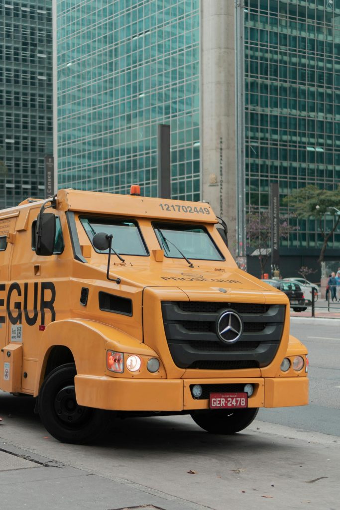 pexels-photo-14119497-14119497 Yellow armored truck on a downtown street with modern buildings in the background.